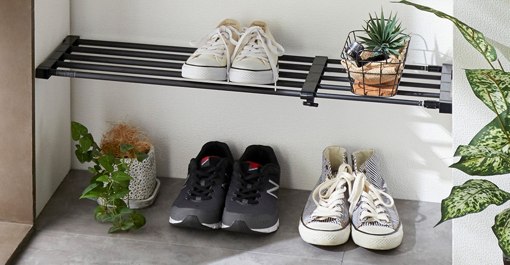 黑白色調的置物架上擺放著兩雙帆布鞋，下方地面上也有兩雙運動鞋和一盆綠色植物，右側有大型室內植物。