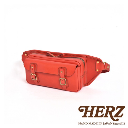 紅色皮革騎士隨身斜背包，配有兩個黃銅色帶扣的翻蓋前袋，上方有拉鍊開口，可調節的皮革腰帶。