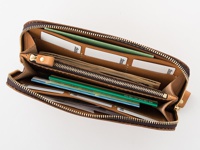 職人手作皮革大容量拉鍊長夾，呈現溫潤的淺棕色皮革，內部結構清晰，可見多個隔層、卡槽，並裝有紙鈔、卡片及綠色筆。拉鍊採用黃銅色金屬，質感良好。