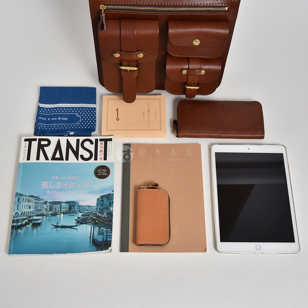 咖啡色皮革三口袋三用後背包，搭配藍色印花手帕、淺棕色筆記本、咖啡色長夾、淺棕色鑰匙包及白色平板電腦，整體以簡潔的佈局呈現。