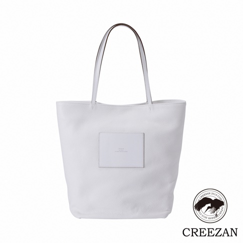 白色皮革大容量肩背托特包，正面中央有一個方形皮革標籤，印有品牌資訊。