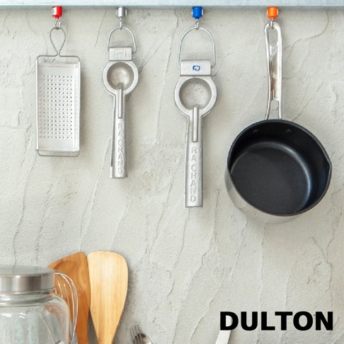 DULTON 品牌下的工業風廚房掛架，展示著不同用途的廚房小工具，包含一個刨絲器、兩個圓形開罐器，以及一個小型湯鍋，掛在灰色的水泥牆上。