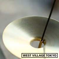 黃銅製的線香架，圓形盤狀設計，中央有一個圓孔，一根細長的黑色線香從孔中穿過，線香架表面呈現拉絲質感，光澤溫潤。