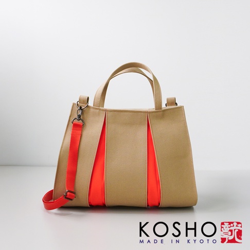 卡其色棉帆布扇形托特包，側面裝飾有鮮豔的橘紅色布料，配有可拆卸的橘紅色織帶肩帶和兩個頂部提把。