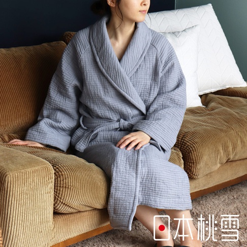 淺灰色雙面紗布浴袍，立體織紋，輕質材質，附腰帶，女性穿著，坐於褐色沙發上。
