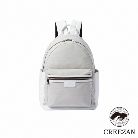 白色與淺灰拼接的CREEZAN品牌後背包，採用帆布材質搭配皮革飾邊，配有雙肩帶與頂部手提把，正面附有拉鍊前袋與小型品牌標籤，整體外觀呈現簡約優雅的設計風格，右下方印有品牌圓形徽標。