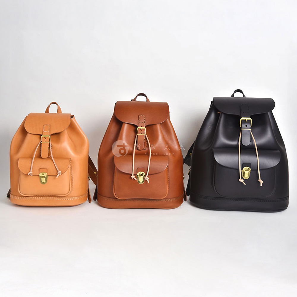 三款職人手作皮革經典後背包，分別為淺棕色、棕色和黑色，皆採用柔軟皮革材質，設計簡約，配有束繩開合與金屬鎖扣，適合日常攜帶。