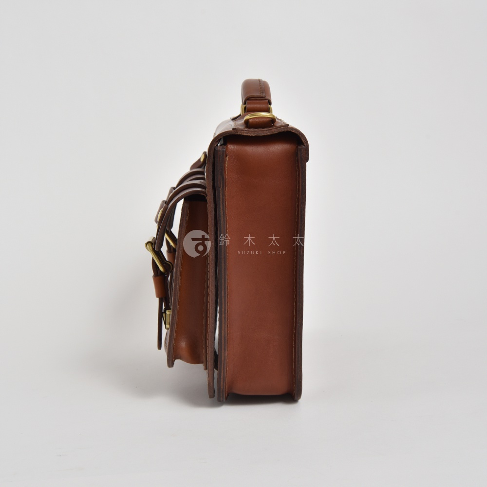 棕褐色皮革雙口袋兩用單肩包，側邊視角，具備手柄、雙口袋設計及金屬扣環，以簡約白色背景呈現。