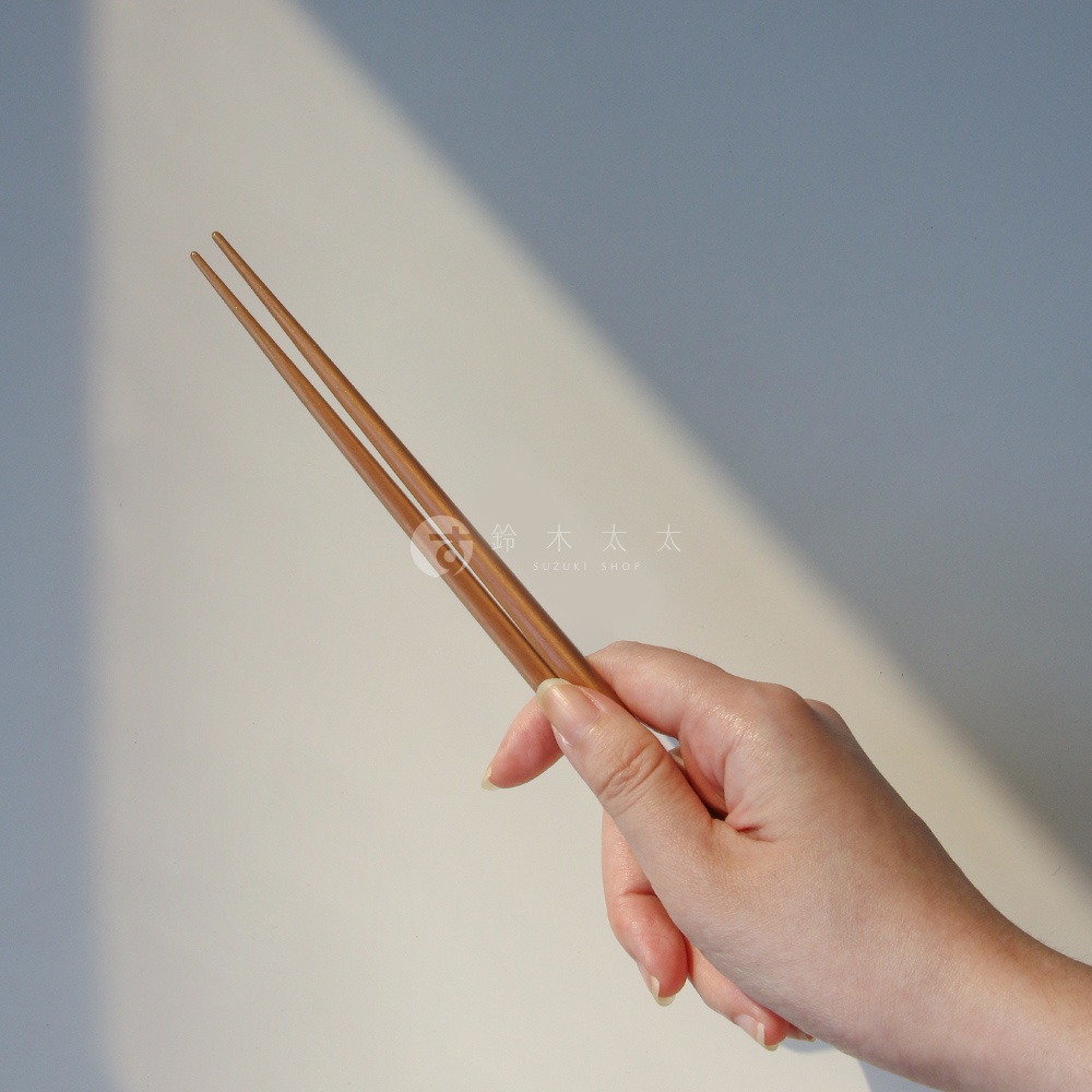 一雙淺棕色原木筷子，由細長的圓柱形木材製成，頂端尖細，由一只手握持。