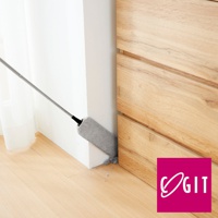 灰色伸縮式地板除塵縫隙清潔刷，末端有灰色纖維刷頭，正在清潔牆角縫隙，旁邊是木紋櫃體與白色牆面。