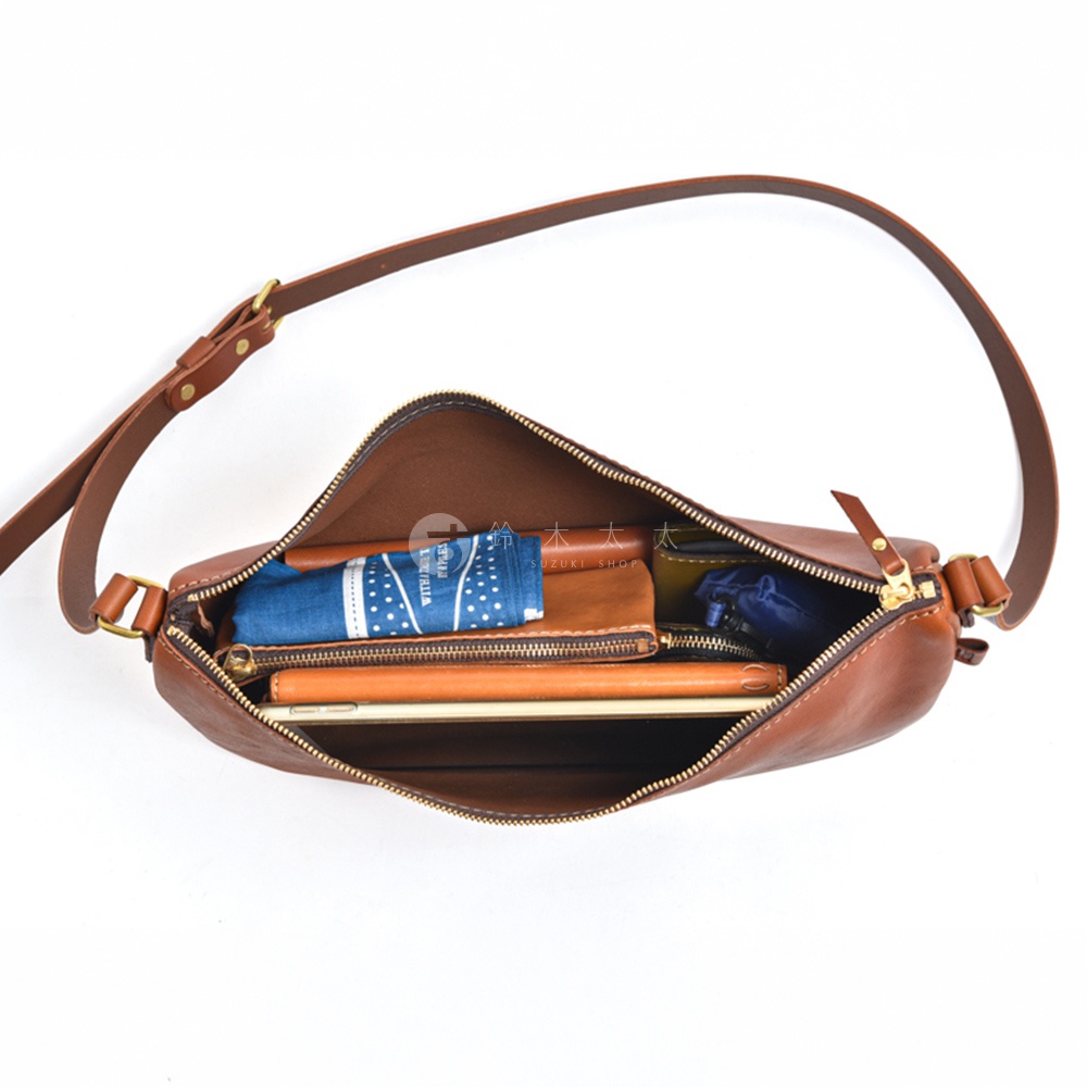 日本HERZ職人手作皮革半圓馬鞍包，打開的包包內可見藍色方巾、皮革錢包、手機等物品，包包為棕色皮革材質，以平視角度拍攝。