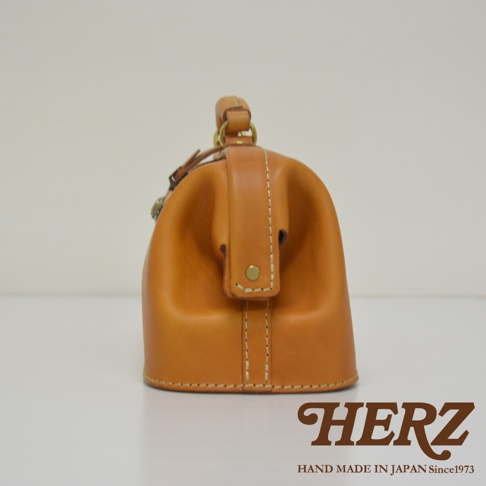 職人手作皮革長型迷你醫生包 CW-106，採用天然皮革材質，呈現經典的醫生包造型。包身為圓潤飽滿的廓形，搭配頂部提把與金屬釦環，展現復古質感。縫線清晰，結構穩固，整體色澤為溫暖的焦糖棕色。