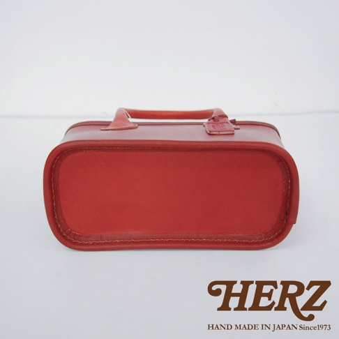 紅色皮革製的職人手作輕巧散步手提包，帶有圓潤的提把，包身側面和底部以車線縫合，展現細緻的手工藝。