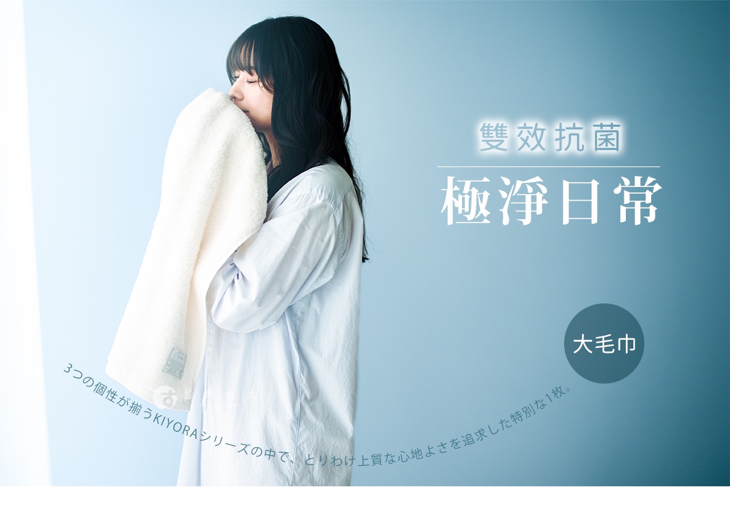 一位女性穿著淺藍色襯衫，雙手捧著一條柔軟的白色大毛巾並輕貼在臉頰旁，呈現出舒適且潔淨的意象。背景為柔和的漸層藍色，畫面右側標示著大毛巾字樣，並呈現極淨日常與雙效抗菌的產品主題，下方文字說明此為KIYORA系列中追求極致舒適感的特別款式。