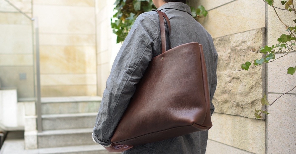 職人手作皮革4口袋極簡托特包 T-3，採用光滑棕色皮革製成，搭配同色系皮革提把，包款簡潔大方，適合日常攜帶。