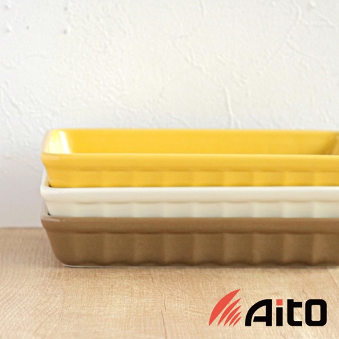 堆疊擺放的美濃燒釉彩萬用長方烤盤，從上至下顏色分別為亮黃色、米白色與淺褐色。烤盤為陶瓷材質，側邊有立體溝紋裝飾，造型簡潔實用。