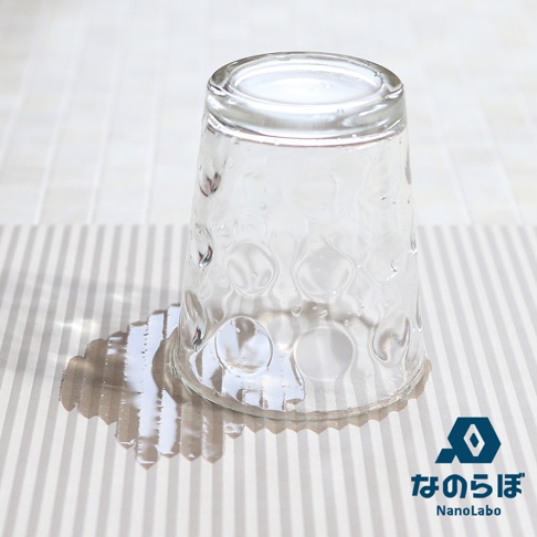 透明玻璃杯倒扣在條紋珪藻土墊上，杯身有水滴和氣泡紋路，杯底周圍有水漬。