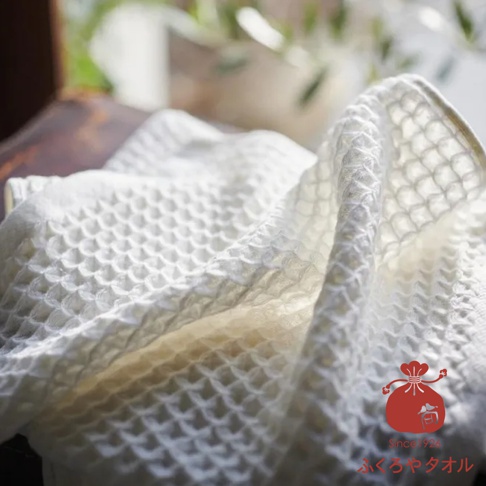 一條白色格紋方巾，質地柔軟，放在深色木桌上，背景模糊。