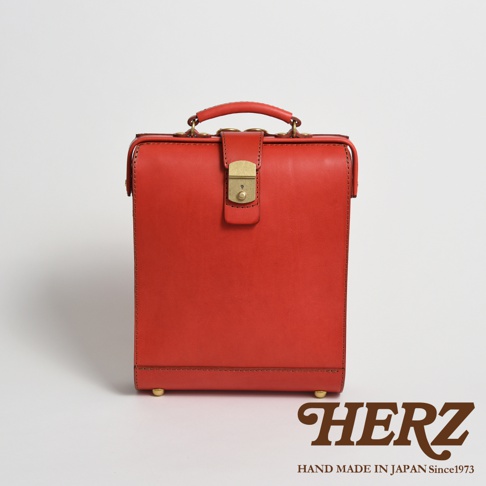 職人手作紅色皮革杜勒斯商務後背包，配有金色鎖扣和提把，底部有四個金色腳釘。