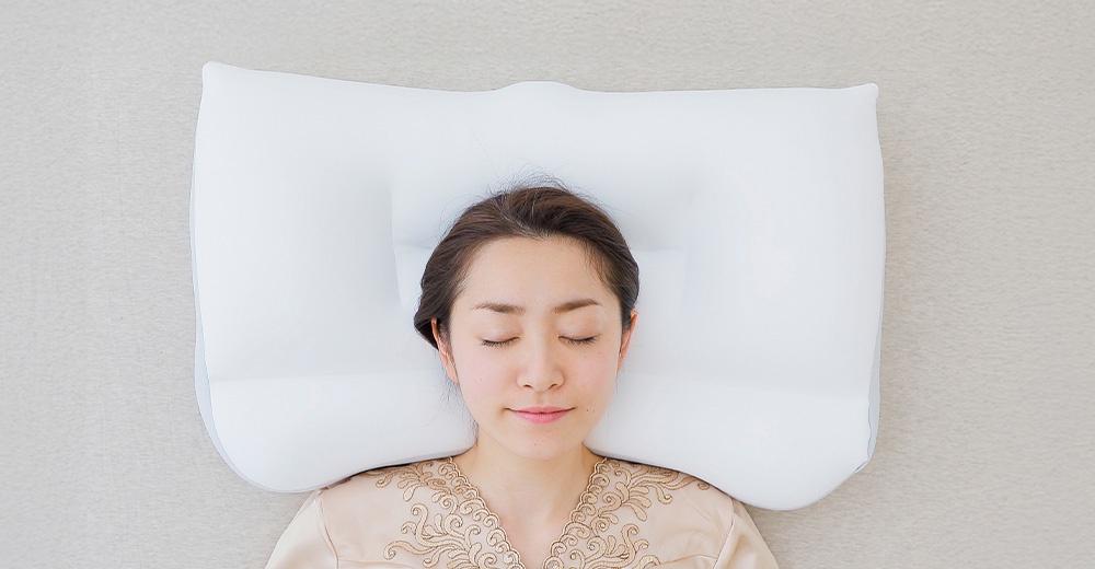 一名女子仰臥在白色枕頭上，閉著眼睛，頭部居中，背景是米色的床鋪。