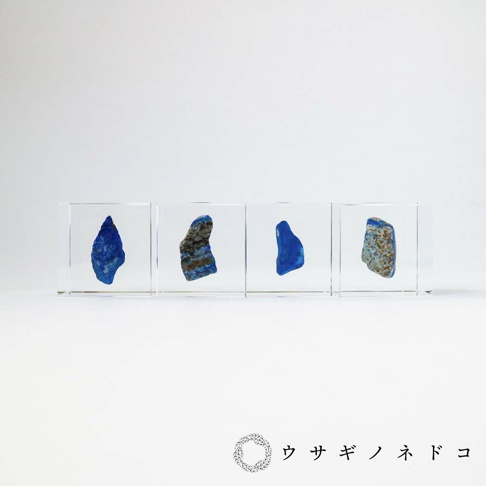 四個透明立方體展示著不規則形狀的青金石礦石，呈現深淺不一的藍色，部分伴有金色或褐色的斑紋。