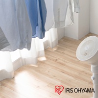 白色直立式落地換氣風扇，旋鈕式操作，扇葉為白色螺旋狀，搭配木紋地板和白色窗簾，上方懸掛著幾件藍色與白色條紋的襯衫。