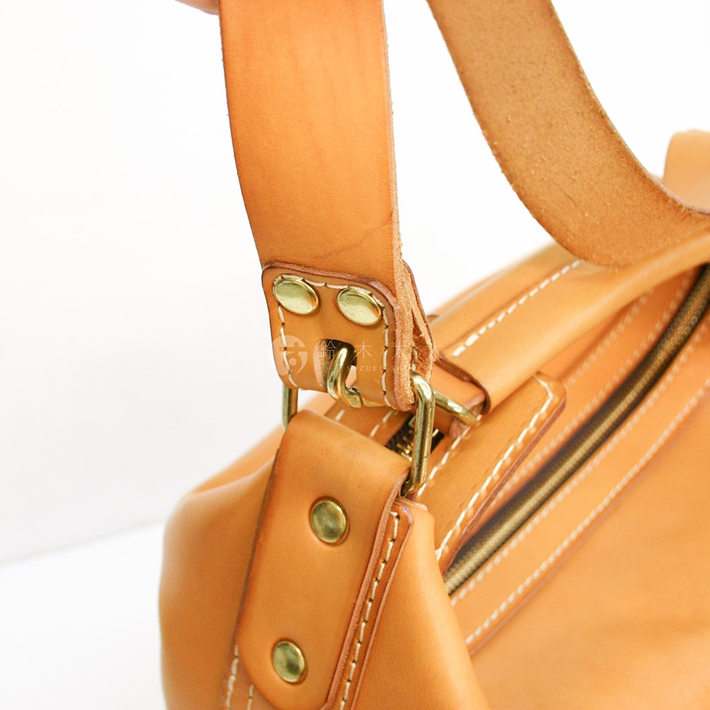 淺棕色皮革手作單肩波士頓包，特寫其厚實的皮革材質、金屬釦環與車縫細節，展現精緻工藝。