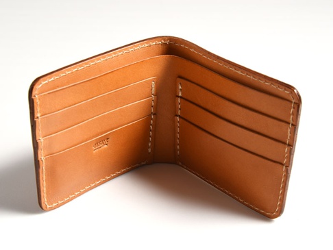 棕褐色皮革雙折短夾，內部有四個卡槽，右側有品牌壓印標誌，縫線為白色。