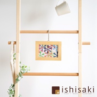 木質牆面收納架，懸掛著一個淺木色相框，框內是色彩繽紛的花朵圖案。架子上方掛著一個白色馬克杯，左側懸掛著一個米白色帆布袋，架子旁有綠色植物點綴。