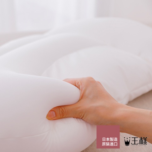 手正按壓白色柔軟的舒肩枕，枕頭表面有明顯的凹陷，呈現蓬鬆的材質感。