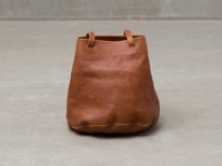 一個棕色皮革抽繩包，有兩個短提把，底部有波浪邊設計，放置在灰色背景上。