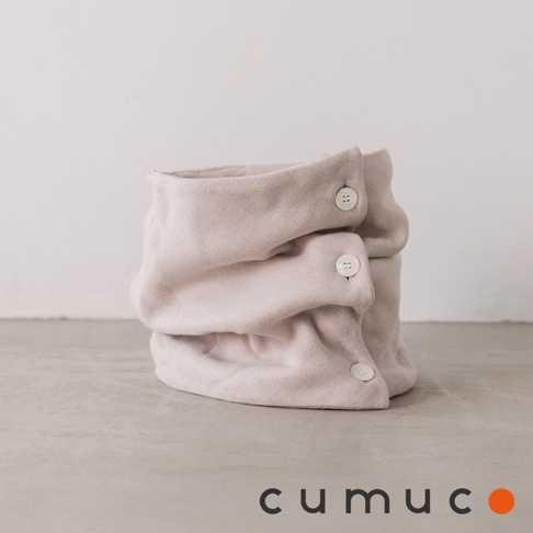 CUMUCO品牌標誌旁，一個淡米色、柔軟的八層紗頸套堆疊著，頸套上有三個對稱的小白色鈕扣細節，背景為淺色牆壁和灰色水泥地面。