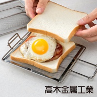 銀色不鏽鋼網烤吐司夾，夾著兩片吐司、培根和煎蛋，另一片吐司由雙手持握準備蓋上。