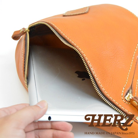 職人手作皮革多功能收納斜背包，橘棕色皮革，拉鍊開口展示內部空間，可放入平板電腦。