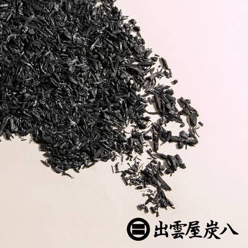 一堆散落的黑色木炭碎屑，呈現不規則的長條形狀，部分堆疊，部分分散在淺色背景上。