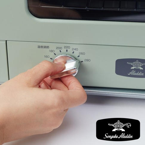 手正在操作復古多用途烤箱的銀色溫度調節旋鈕，旋鈕旁標示著160至280度的溫度刻度。烤箱機身為淺綠色，右側印有Aladdin的深藍色Logo。