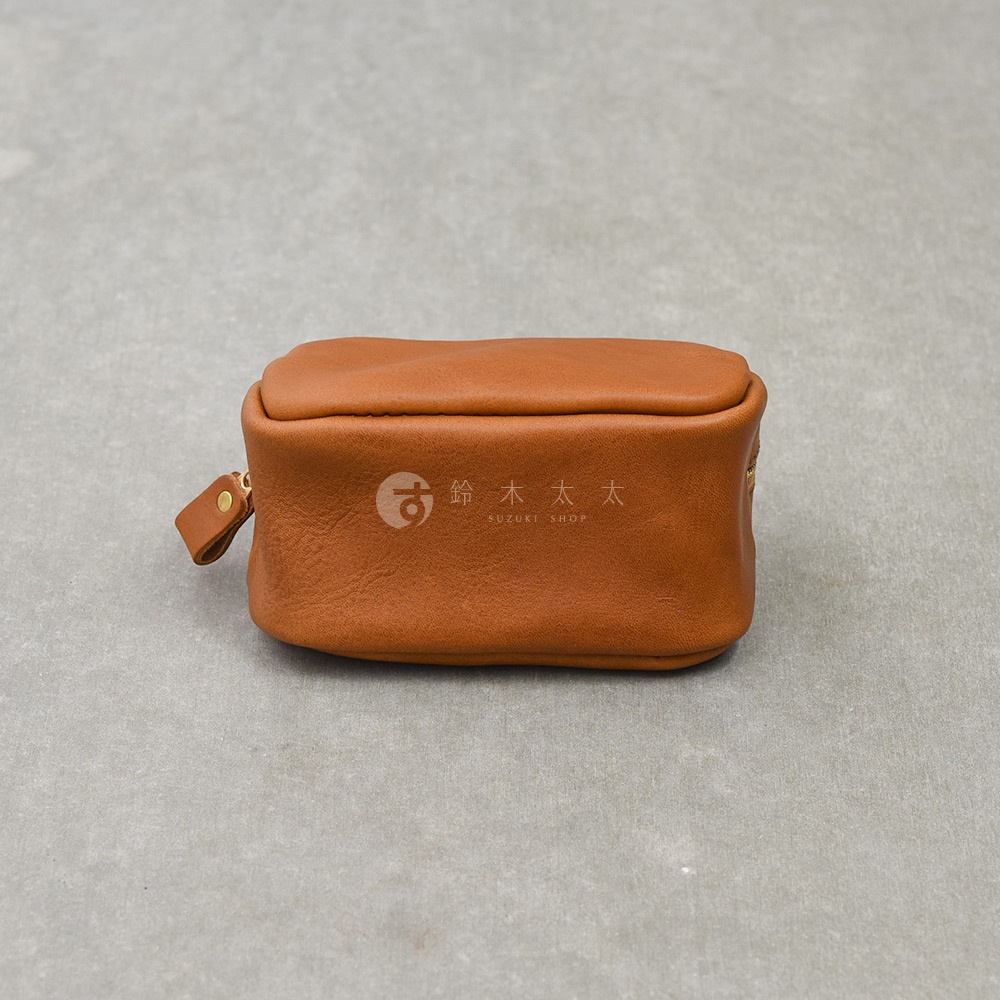 一個棕色的HERZ手工皮革拉鍊收納包平放在灰色背景上，包身正面印有SUZUKI SHOP的商標文字，外觀簡約並設有皮革拉鍊環。