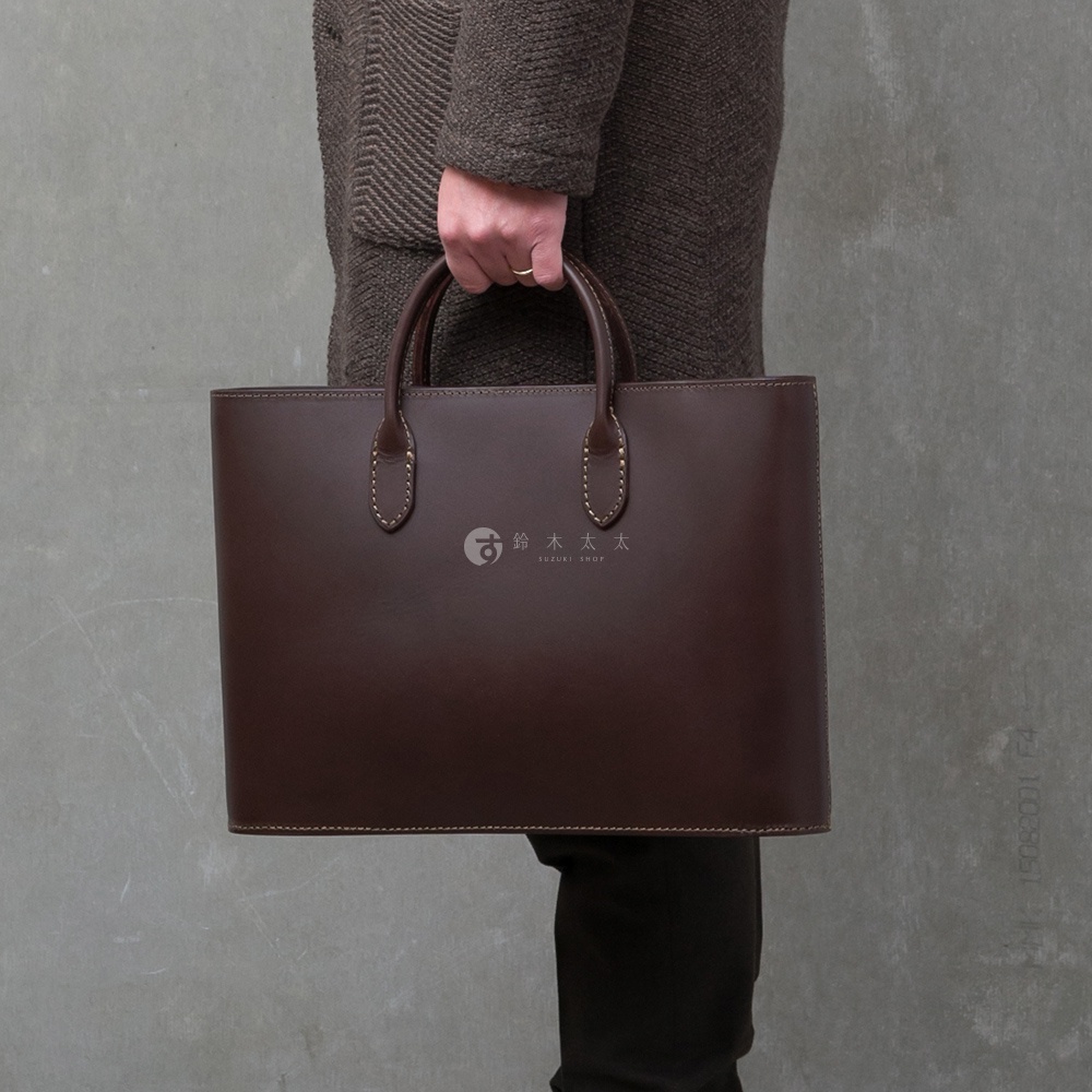 深棕色皮革薄型公事包，配有雙提把及縫線細節，包身中央有「鈴木」圖案與文字Logo。
