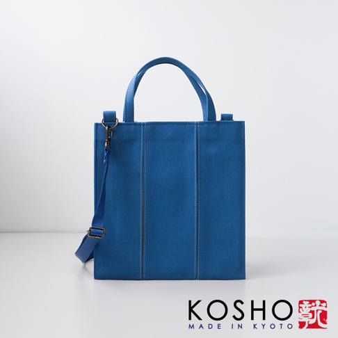 藍色棉帆布扇形托特包，有兩個提把和一條可拆卸肩帶，包身有垂直縫線裝飾。