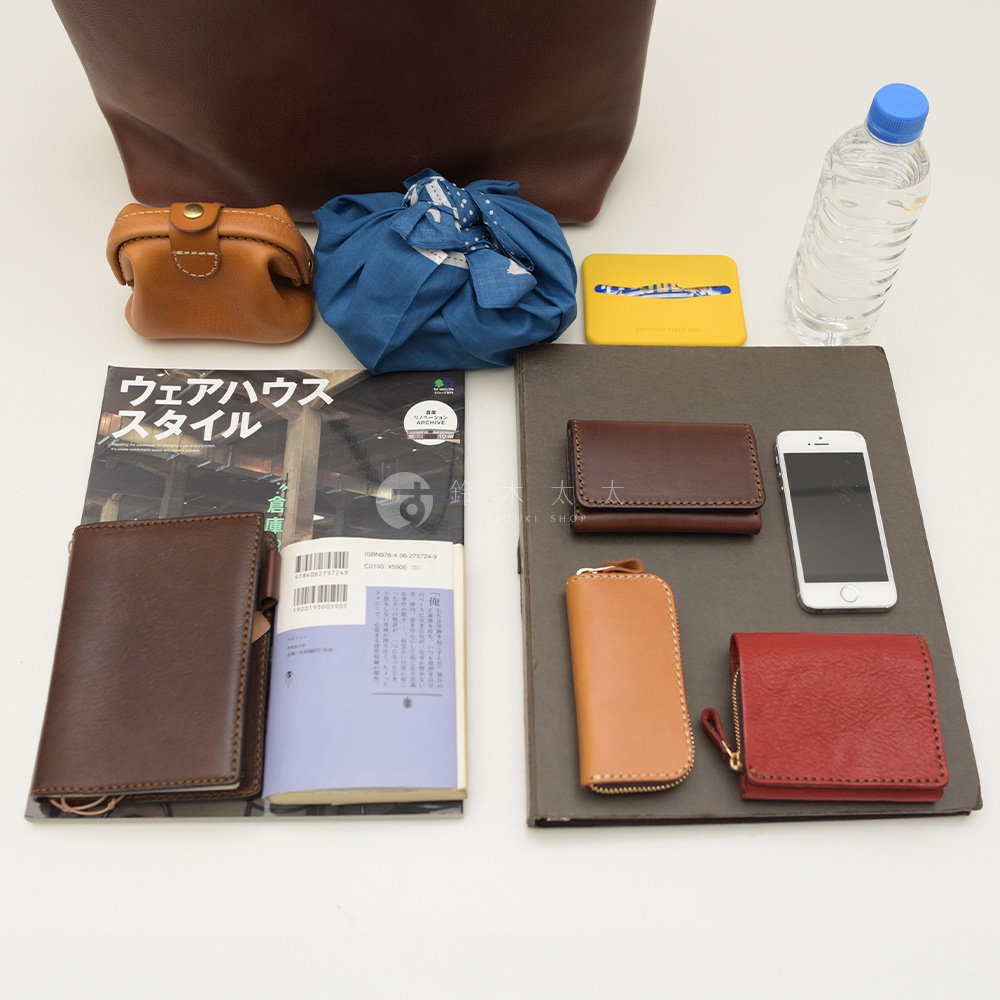 深棕色皮革托特包，內含一個棕色皮革零錢包、一個藍色布包、一個黃色方形物品、一本雜誌、一本深棕色皮革筆記本、一個棕色皮革短夾、一個棕色皮革鑰匙包，一個紅色皮革短夾，以及一瓶水。