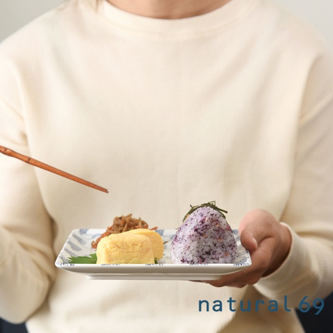 一個裝有玉子燒、紫米飯糰和配菜的方形陶瓷餐盤，盤緣飾有藍色葉紋。