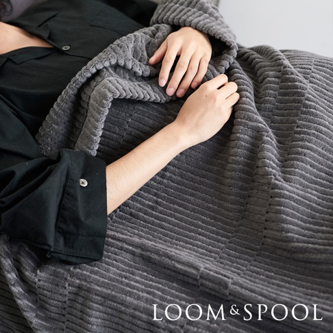 一件深灰色、立體直紋的微厚單人純棉毯，覆蓋在身穿黑色襯衫的人身上，展現其柔軟的紋理。