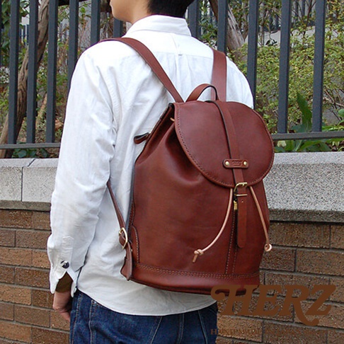 咖啡色皮革單扣束口後背包，採用職人手作工藝，配有可調節肩帶和金屬扣環，展現經典復古風格。
