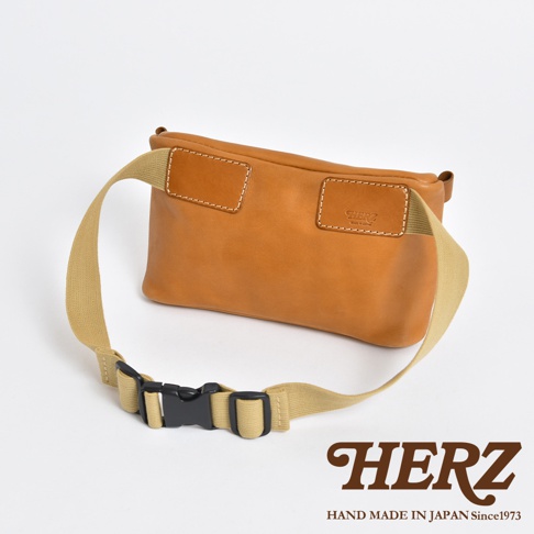 職人手作皮革兩用腰掛斜背包，淺棕色牛皮材質，附可調節的米色織帶與黑色扣環，包身有白色縫線裝飾，右上方壓印有品牌Logo。
