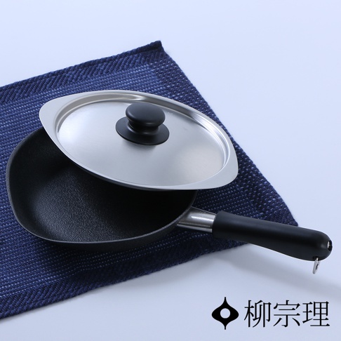 黑色雙網紋單手鐵鍋，附有金屬鍋蓋，鍋蓋上有黑色圓形把手，鍋柄為黑色，置於藍色紋理布上。