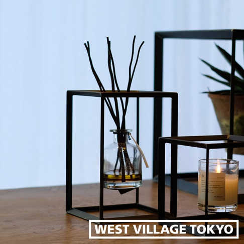 黑色鐵製長方型展示架，中間懸吊著一個玻璃擴香瓶，瓶內有擴香枝和液體。右側為一個點燃的香氛蠟燭，置於另一個黑色鐵製架上。