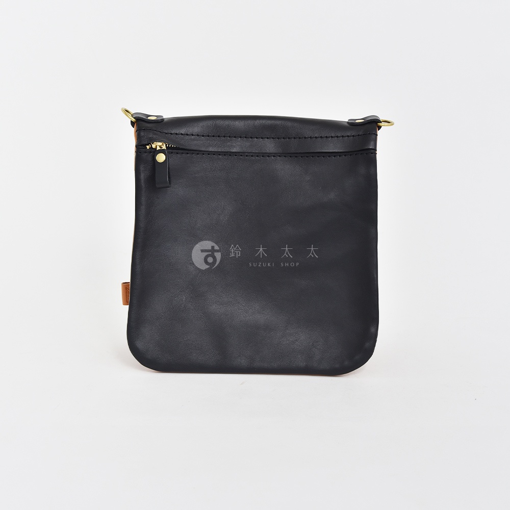 黑色皮革翻轉直式斜背包，正面中央有「鈴木太太」品牌標誌，頂部有拉鍊開口及金色拉鍊頭，側邊有皮革標籤。