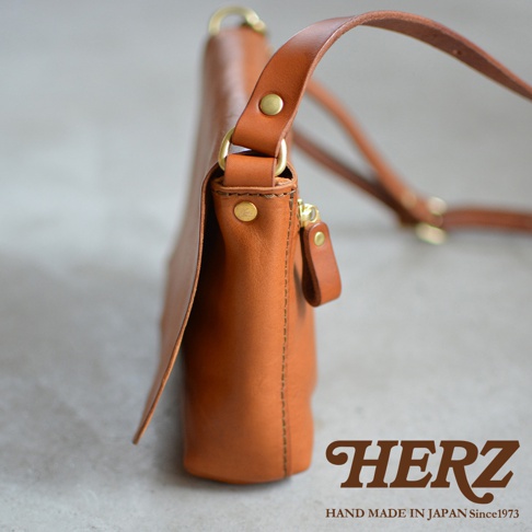 一個棕褐色皮革製成的斜背包，背包側面有拉鍊和品牌標誌。