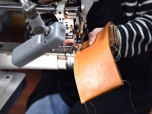 職人手作皮革直式卡片收納雙折短夾，以棕褐色皮革製成，正在工業縫紉機上進行縫合，展現精湛工藝。