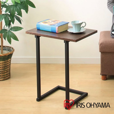 簡約時尚小邊桌 SDT-45，桌面為深棕色木紋，搭配黑色金屬C型桌腳。桌面上擺放一本藍色封面的書和一個淺藍色杯子與杯墊。背景為淺木紋地板和白色牆面，左側有一盆綠植。